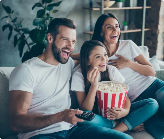 A family sitting on a couch enjoying pop corn and watching TV