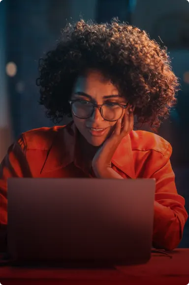 A Woman in red shirt with glasses working on laptop.